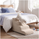 Kleiner weißer Hund läuft die beige Haustiertreppe neben dem Bett in einem hellen Schlafzimmer mit Spielzeug und einem geflochtenen Korb hinunter.