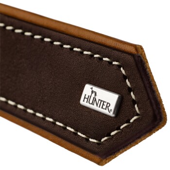 Nahaufnahme eines braunen Lederhundehalsbands mit weißen Nähten und einem silbernen 'HUNTER'-Logoanhänger.