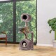 Ein plüschiger, mehrstöckiger Katzenbaum in einem modernen Raum, mit einer braunen getigerten Katze, die auf einem Regal entspannt, und einer weißen Katze, die aus einem unteren Versteck herauslugt.