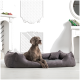 Ein brauner Hund, der auf einem plüschigen grauen Hundebett in einem stilvollen Raum mit weißen Wänden und dekorativen Elementen entspannt.