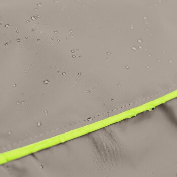 Nahaufnahme einer wasserabweisenden Haustierjacke in Grau mit einem leuchtend gelben Reißverschluss, die Wassertropfen auf dem Stoff zeigt.