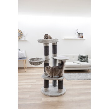 Zwei graue Katzen auf einem mehrstufigen grauen Kratzbaum in einem modernen Wohnzimmer mit weißem Sofa und Holzboden.