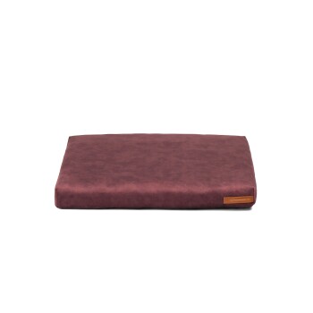 Ein rechteckiges Haustierbett in einem satten Burgunderrot, mit einer glatten Textur und einem kleinen Lederetikett mit dem Namen der Website.