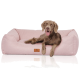 Ein glücklicher brauner Hund, der auf einem weichen rosa Haustierbett mit einem Lederetikett sitzt, auf dem "KNUFFELWUFF" steht.