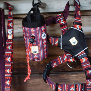 Ein farbenfrohes Hundegeschirr und eine Leine von Woolly Wolf, mit einem geometrischen Muster in Rot, Schwarz und Weiß, hängen an einer Holzwand.