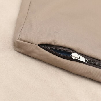 Nahaufnahme eines beigen Haustierbettes mit einem Reißverschlussdetail, das auf einer weichen, hellen Oberfläche ruht.