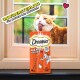 Eine verspielte orange Katze mit blauen Augen streckt ihre Zunge neben einer Packung Dreamies Meaty Sticks, die mit "90% FLEISCH" beschriftet ist.