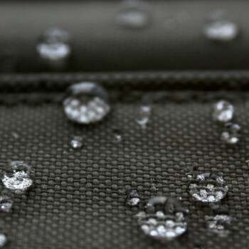 Nahaufnahme von Wassertropfen auf einem strukturierten dunklen Stoff, der die wasserabweisenden Eigenschaften des Stoffes zeigt.