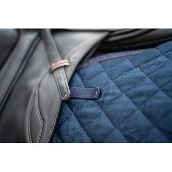 Nahaufnahme eines schwarzen Ledersattels mit einem marineblauen, gesteppten Sattelpad, das einen Riemen und einen dekorativen roten Akzent aufweist.