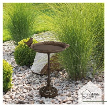 Ein dekorativer Vogelbad mit einer Vogelstatue am Rand, in einem Garten mit grünem Gras und Steinen, mit dem Logo 'wildlife home.'