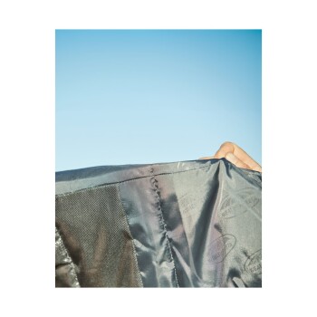 Eine Nahaufnahme einer Hand, die eine schwarze Haustierjacke gegen einen klaren blauen Himmel hält, wobei die Textur und die Nähte des Stoffes zur Geltung kommen.