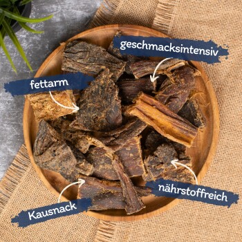 Ein Holzbrett mit Hundekau-Snacks, beschriftet auf Deutsch: "fettarm", "geschmacksintensiv", "nährstoffreich" und "Kausnack."