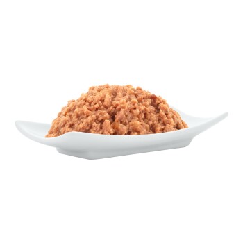 Ein Haufen Haustierfutter in einer weißen Schüssel, mit einer weichen, klumpigen Textur und einer rosa-braunen Farbe.