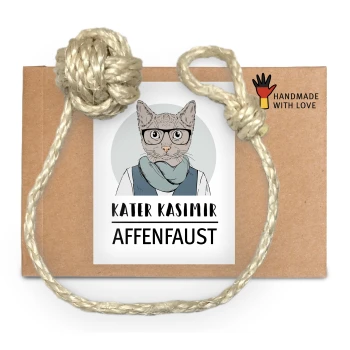 Ein braunes Kartonpaket, das mit einem Seil gebunden ist, mit einem Etikett, das "KATER KASIMIR AFFENFAUST" liest und einer Grafik einer Katze.