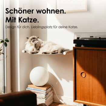 Flauschige Katze auf einer Wandhängematte neben Plattenspieler und Lampe; sichtbarer Text: "Schöner wohnen. Mit Katze."