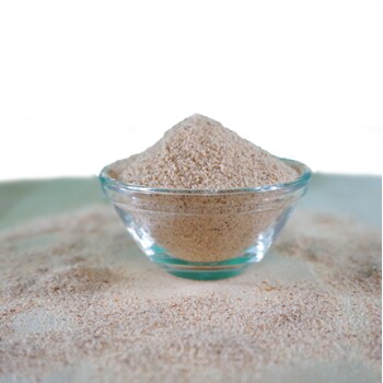 Eine klare Glasschüssel, gefüllt mit hellbraunem Haustierergänzungspulver, umgeben von einer Staubschicht des gleichen Pulvers auf einer Oberfläche.