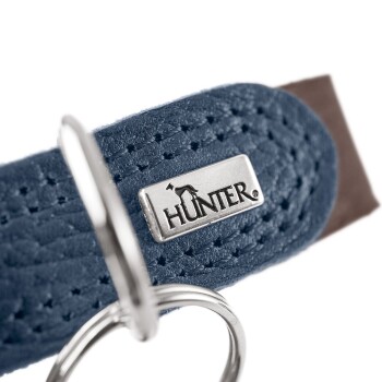 Nahaufnahme eines blauen Hundehalsbands mit einem silbernen "HUNTER"-Logo und einem metallischen D-Ring zur Leinenbefestigung.