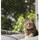 Eine entspannte getigerte Katze, die auf einem grauen Kissen liegt, mit einem grünen, blättrigen Hintergrund und einem Schutznetz im Vordergrund.
