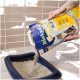 Een persoon giet Biokats Classic 3in1 kattenbakvulling uit een blauwe zak in een donkerblauwe kattenbak, met een lichte tegelachtergrond.
