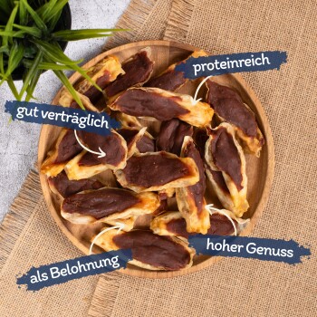 Eine Holzschüssel mit Hundeleckerlis, beschriftet auf Deutsch: "gut verträglich", "hoch in Protein", "als Belohnung" und "hoher Genuss", mit einer grünen Pflanze im Hintergrund.