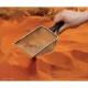 Eine Hand, die eine Metallschaufel über orangefarbenem Sand hält, mit kleinen Trümmern, die in der Schaufel sichtbar sind, was auf Haustierpflege oder Habitatpflege hindeutet.