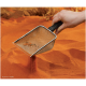 Eine Hand, die eine Metallschaufel über orangefarbenem Sand hält, mit kleinen Trümmern, die in der Schaufel sichtbar sind, was auf Haustierpflege oder Habitatpflege hindeutet.