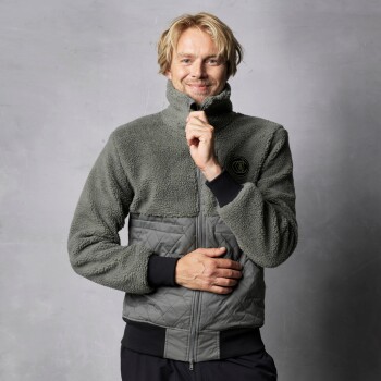 Eine Person in einer gemütlichen, grauen Fleecejacke mit einem gesteppten unteren Abschnitt, die vor einem neutralen Hintergrund steht.