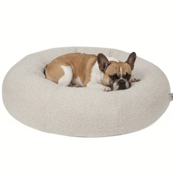 Runder, plüschiger Haustierbett in einem hellbeigen Farbton mit einem gesteppten Design, das ein kleines Etikett mit der Aufschrift "PAW WOW" trägt.