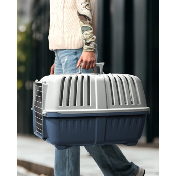 Person trägt blau-graue Hartplastik-Transportbox mit belüftetem Deckel und vorderer Metalltür am Griff.