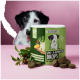 Ein Behälter mit "Gras & Kotfresser Drops" (350g) mit dunkelbraunen Tropfen, die herumgestreut sind, und einem Hund, der im Hintergrund neugierig schaut.