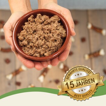 Eine Person hält eine braune Schüssel mit Hundefutter, umgeben von Hundeleckereien. Ein Abzeichen liest "Beste Qualität - 15 Jahre."