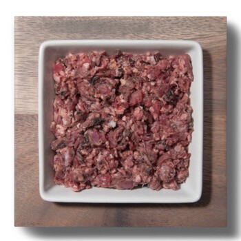 Ein quadratisches weißes Geschirr gefüllt mit fein gehacktem rohem Fleisch, das eine Mischung aus roten und braunen Farbtönen zeigt, auf einer Holzoberfläche platziert.