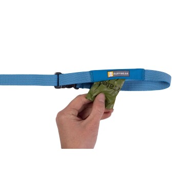 Eine Hand zieht einen grünen Abfallbeutel von einer blauen Hundeleine mit einem Ruffwear-Logo, was das praktische Design der Leine zeigt.