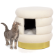 Eine graue Katze steht neben einem plüschigen, cremefarbenen Katzenbett mit runder Form und einem goldenen Sockel, das einen gemütlichen Eingang hat.