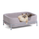 Eine flauschige, hellfarbige Katze liegt bequem in einem stilvollen grauen Haustierbett mit einem Metallrahmen und zeigt ein gemütliches Design.