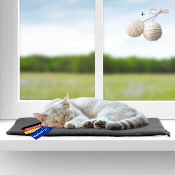 Weiße Katze schläft auf einer schwarzen Matte am Fenster mit den Etiketten „Deutsche Marke“ und „Made in EU“ und zwei darüber hängenden Seilbällen.