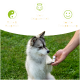 Ein flauschiger grau-weißer Hund sitzt auf Gras und greift nach einer Hand einer Person, die eine kleine Flasche mit beruhigenden Effekten auf Deutsch hält.