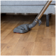 Eine Staubsaugerdüse ist auf einem Holzboden positioniert, teilweise sichtbar unter einem grauen Sofa.