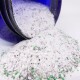 Nahaufnahme eines blauen Glases, das eine Mischung aus weißem und grünem Haustierstreu verschüttet, mit kleinen schwarzen und grünen Granulaten, die auf einer weißen Oberfläche sichtbar sind.