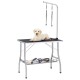 Ein hellfarbener Labrador-Welpe liegt auf einem Grooming-Tisch mit einem Grooming-Arm und Gurten, umgeben von Grooming-Werkzeugen auf einem unteren Regal.