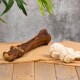 Ein Hundekau-Knochen und ein geknotetes Seilspielzeug werden auf einer Juteschicht präsentiert, mit einem strukturierten grauen Hintergrund und einer Holzoberfläche.
