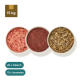 Drei Pakete Haustierfutter, beschriftet mit "Rinderpansen grün," "Rind-Komplett Extra," und "Rinderkomplettfleisch," neben Schalen mit rohem Fleisch.