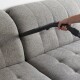 Eine Hand hält eine Staubsaugerdüse und reinigt ein graues, gepolstertes Sofa mit einem gepolsterten Design.
