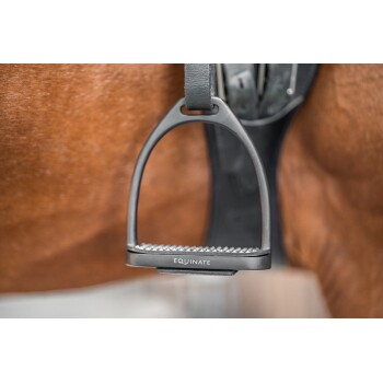 Nahaufnahme eines schwarzen Pferdestegs mit dem sichtbaren Text "EQUINATE," der von einem Sattel an der Flanke eines braunen Pferdes hängt.