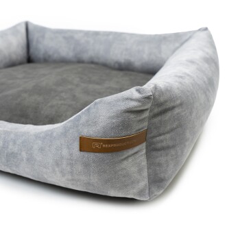 Graues Haustierbett mit einer weichen, plüschigen Oberfläche und erhöhten Rändern, mit einem braunen Etikett, das "RexProduct.com" liest.