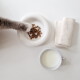 Eine weiße Keramik-Hundeschüssel steht auf einem weißen Tisch neben einer kleinen brennenden Kerze, mit dem flauschigen Schwanz einer Katze im Hintergrund sichtbar.