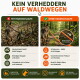 Person in grüner Jacke hält eine orangefarbene Leine, die an einem sitzenden grauen Hund befestigt ist, am Flussufer mit Bäumen.