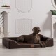 Ein grauer Hund liegt auf einem stilvollen braunen Hundebett in einem hellen, eleganten Raum mit weißen Wänden und dekorativen Elementen.