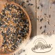 Eine Holzschale mit gemischtem Vogelfutter, einschließlich Sonnenblumenkernen, auf einer Holzoberfläche mit verstreuten Samen und dem Logo "All-Mühle".