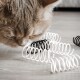 Nahaufnahme einer neugierigen beigen Katze, die bunte Spiralspielzeuge schnüffelt, mit schwarz-weißen Spiralen auf einem Holzboden.